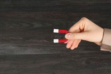 Woman with horseshoe magnet on wooden background, closeup. Space for text
