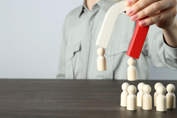 Woman with magnet attracting human figures at wooden table, closeup. Space for text