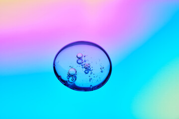 A drop of cosmetic serum on a multicolored background in shades of blue and lilac.