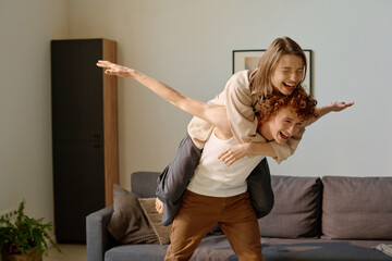 Wide shot of red haired man rising his girlfriend on back, she laughing and screwing up her eyes