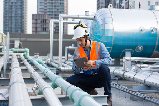 Male engineer work using digital tablet for checks or maintenance in sewer pipes area at construction site. Male plumber working in sewer pipes area at rooftop of building