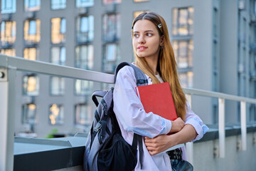 Portrait of young smiling college student girl with backpack textbook, outdoors
