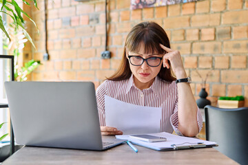 Serious sad middle-aged business woman reading paper letter in coworking cafe