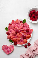Heart shaped pink sweets, fried angel wings, coloured with beetroot. Valentine day romantic breakfast with raspberries, white background, top view.