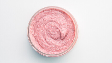 A small pink jar of cream sits on a white background. The cream is a light pink color and he is a lotion or a similar product