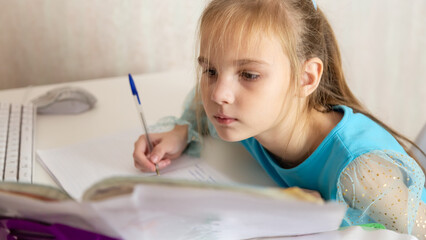 Little school girl sit at table at home write in exercise book prepare homework alone.