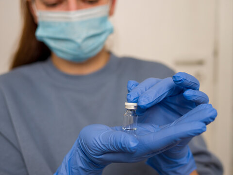 Medical professional wearing surgical mask and blue latex gloves carefully holding glass vial of vaccine, focusing on precision and safety while preparing glass vial of vaccine for medical use  - Powered by Adobe