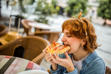 Young ginger girl biting slice of delicious looking pizza.