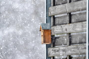 A birdhouse is sitting on a wooden fence in the snow