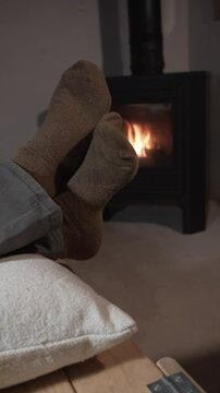 vertical video of barefoot man's feet in brown socks in front of a wood fireplace