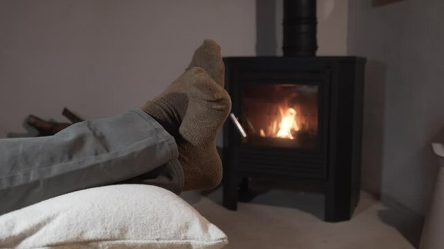 horizontal video of barefoot man's feet in brown socks in front of a wood fireplace