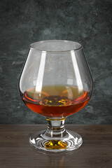Glass of cognac on the wooden table against the wall in grunge style. Bar theme. Dark environment. 3d rendering.
