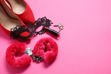 Red fluffy handcuffs, keys, lace mask, shoes and lipstick on pink background, flat lay. Space for...