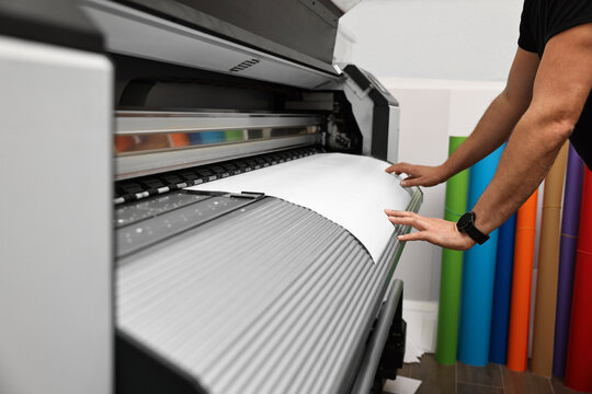 Man using wide-format printer indoors, closeup. Printing house