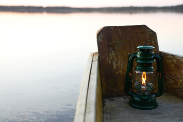 Vintage kerosene lamp in wooden boat near river at sunset