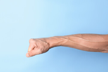 Man with bulging veins on his arm against light blue background, closeup