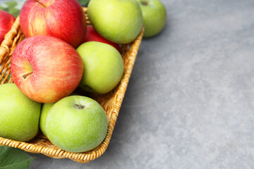 Fresh ripe apples in wicker basket on grey table, closeup. Space for text