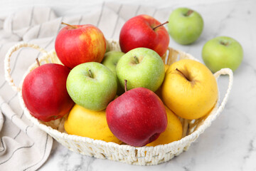 Different ripe apples in basket on white table, closeup