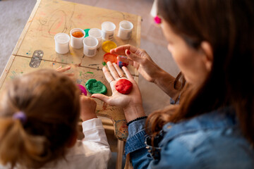 Mother showing her daughter how to play with modeling clay, developing her creativity and motor...