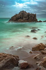 waves crashing against a rock, large rock in the sea with cormorants perched on it