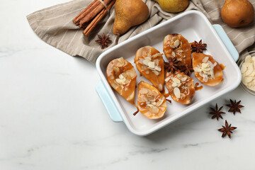 Delicious pears with caramel sauce, almond flakes and spices on white marble table, top view. Space for text