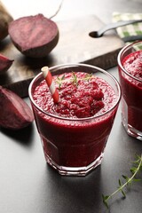 Fresh beetroot smoothie in glass and cut vegetables on grey textured table, closeup