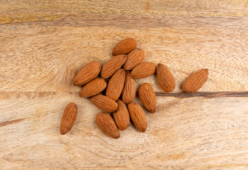 Almonds pile, nut group, whole almond seeds, brown scattered fruit kernels, dry raw nuts on wood