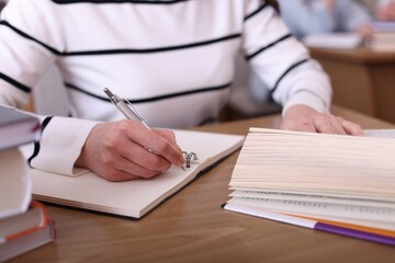 Woman reading book and taking notes at desk in library, closeup