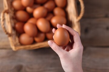 Woman holding raw egg above wooden table, top view