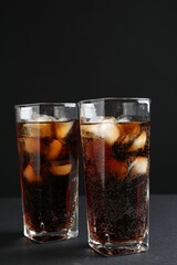 Refreshing cola with ice cubes in glasses on black table, closeup