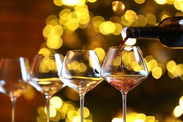 Pouring red wine into glass against blurred lights, closeup. Bokeh effect