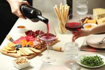 Woman pouring wine into glass at table with different snacks indoors, closeup