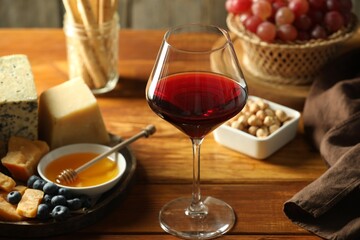 Red wine and different snacks served on wooden table, closeup