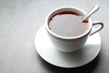 Refreshing black tea and spoon in cup on grey textured table, closeup. Space for text