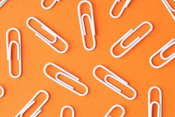 Many paper clips on orange background, flat lay