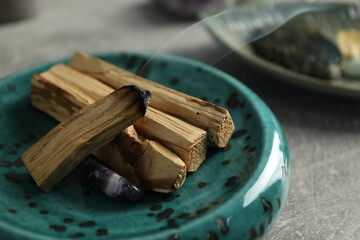 Smoldering palo santo stick and gemstone on light grey table, closeup