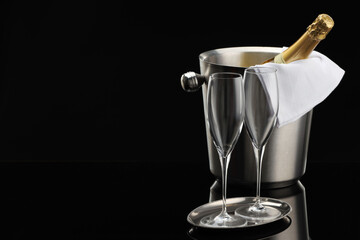 Bottle of sparkling wine in cooler bucket and glasses against black background. Space for text