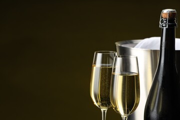 Bottle of sparkling wine, glasses and cooler bucket on brown background, closeup. Space for text