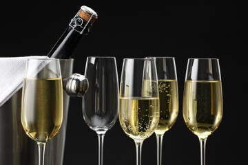 Bottle of sparkling wine in cooler bucket and glasses against black background, closeup