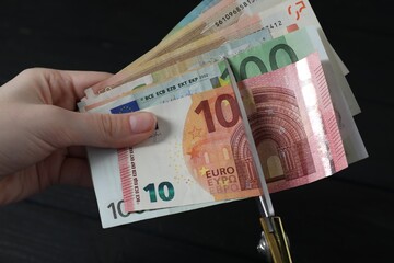 Woman cutting euro banknotes at black table, closeup