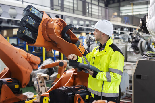 Caucasian worker operates industrial robot arm in a modern factory while looking and smiling to camera