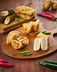 Assorted traditional snacks are presented on a wooden board, highlighting flavors and textures with fresh green and red peppers