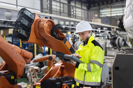 Caucasian worker operates industrial robot arm in a modern factory while looking and smiling to camera