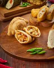 A variety of flavorful snacks, including stuffed pastries and rolls, are arranged appealingly on a wooden platter with greens
