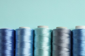 Different spools of sewing threads on light blue background, flat lay. Space for text