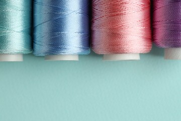 Different spools of sewing threads on light blue background, flat lay. Space for text