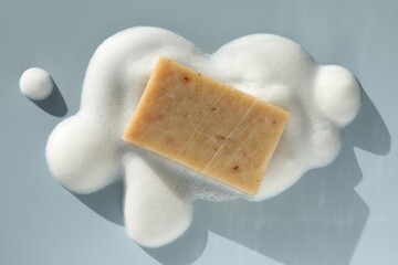 Soap bar with foam on grayish blue background, top view