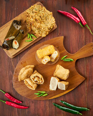 A wooden board displays colorful traditional snacks, surrounded by fresh green and red chili peppers for a vibrant look