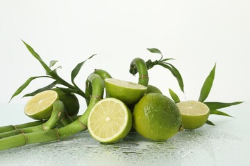 Fresh limes and bamboo stems on wet surface against white background