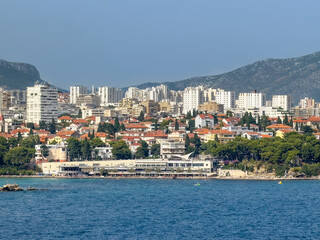 Split, Croatia - July 1, 2024: East side of Uvala Bacvice, small cave called cove. Beach with tourism-related long building. Tall apartment buildings cityscape in back 